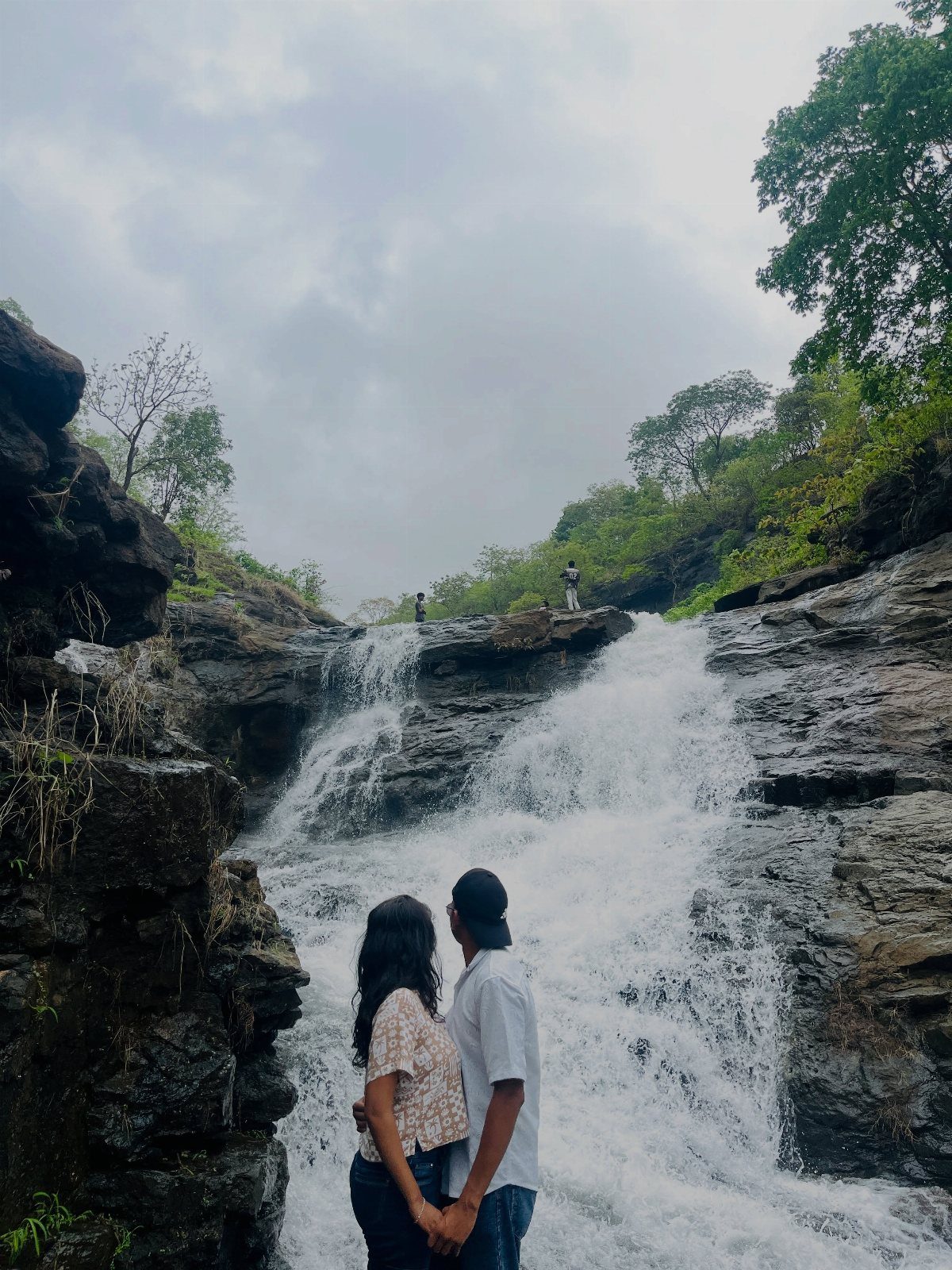 Couple holding hands while looking at a large cascading waterfall in nature.