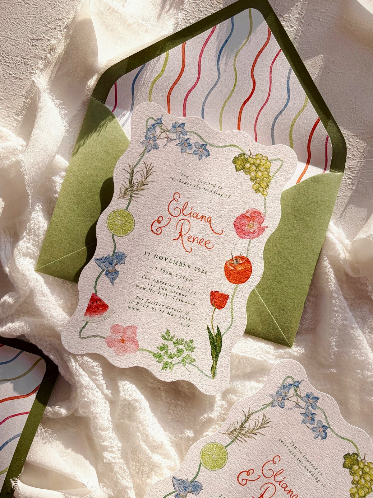 Scalloped wedding invitation with floral illustrations inside a green striped envelope.