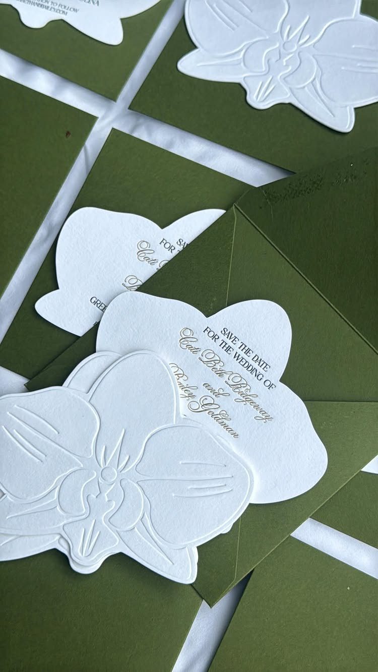 Flower-shaped white wedding invitations with gold text in olive green envelopes