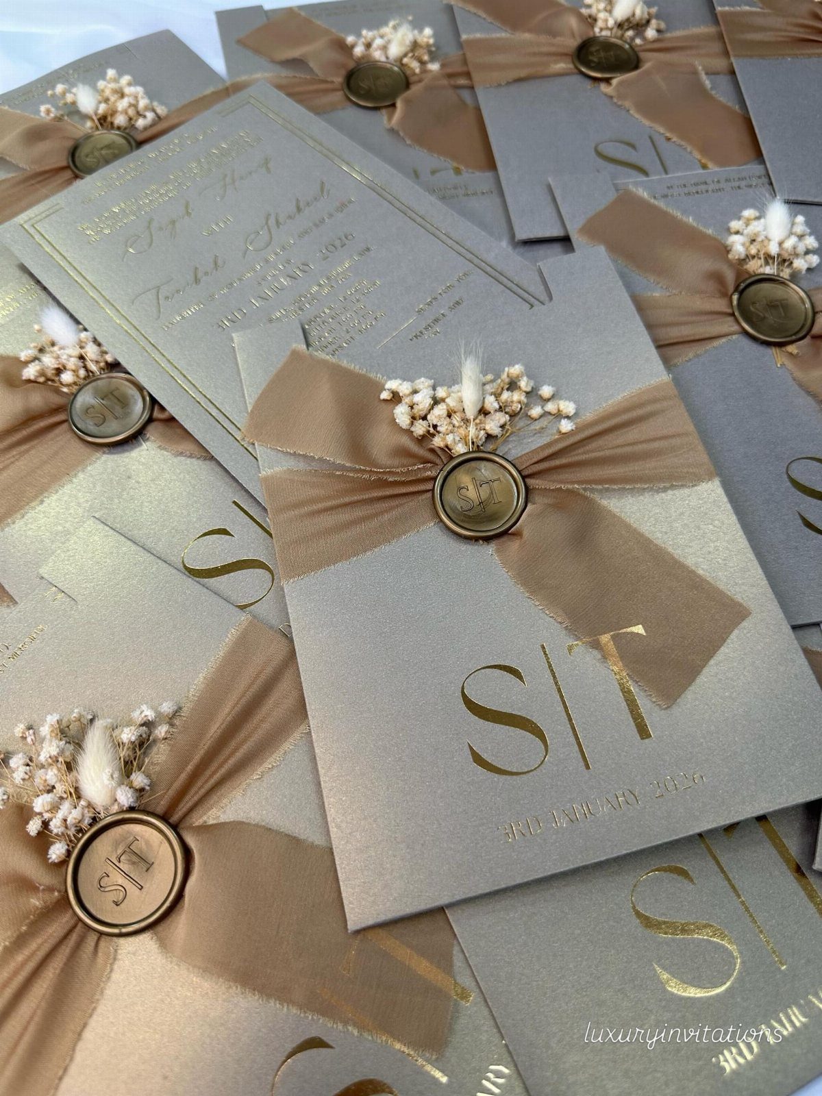 Grey wedding invitations with gold foil text, tan ribbons, and gold wax seals.