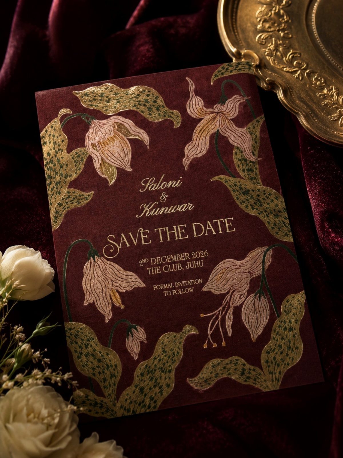 Burgundy save-the-date card with gold foil floral designs on red velvet fabric.