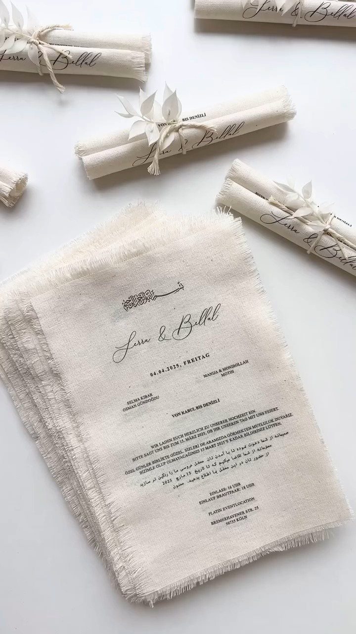Fabric wedding invitations with frayed edges, some rolled and tied with twine.