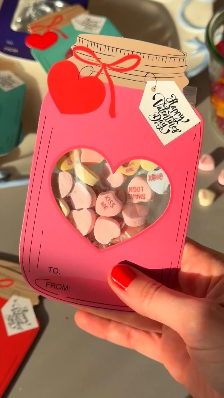 Pink jar-shaped treat bag filled with heart candies held by a hand.