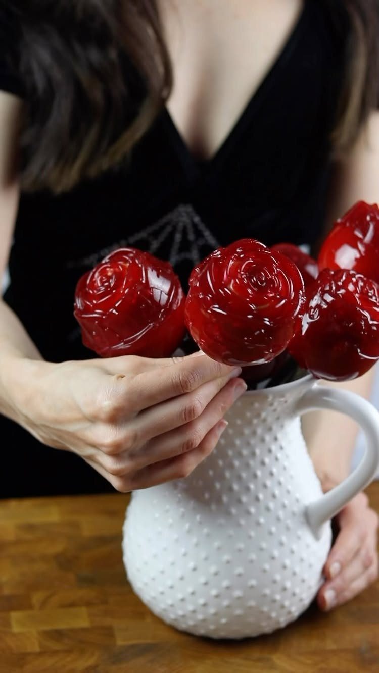 Red candy roses on sticks arranged in a white textured ceramic pitcher.