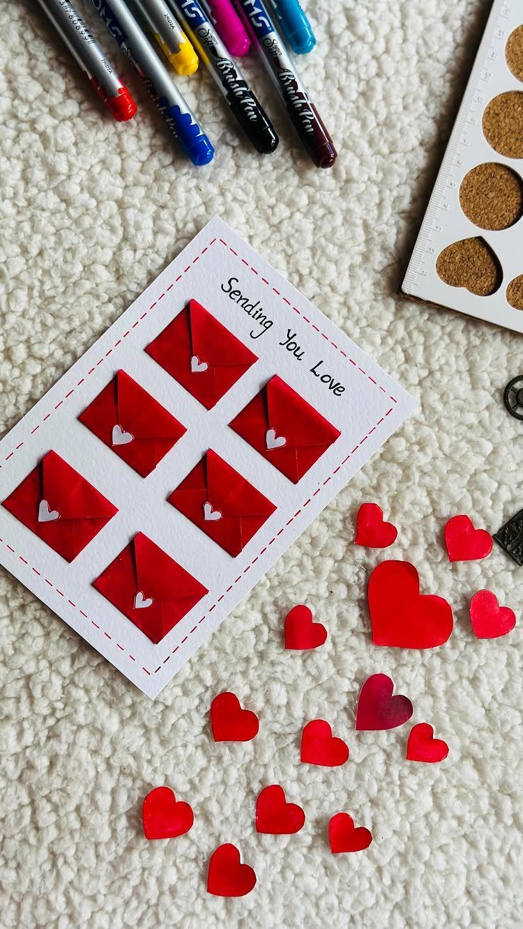 Handmade Valentine's card with red envelopes surrounded by markers and paper hearts.