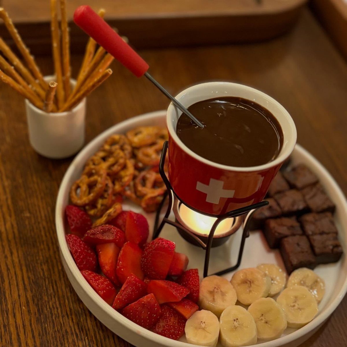 Chocolate fondue pot surrounded by strawberries, bananas, brownies, and pretzels on a platter.