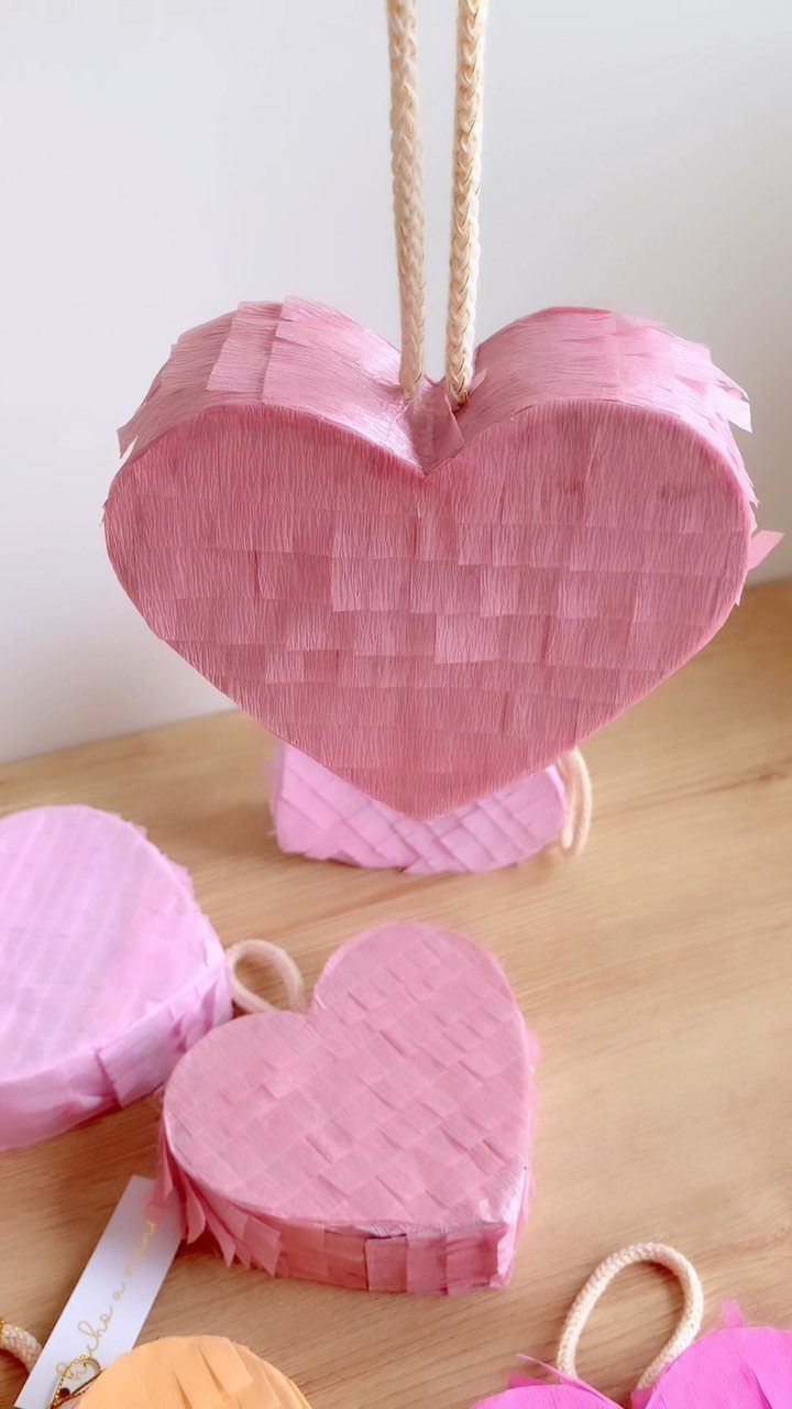 Pink heart-shaped piñatas with fringed paper textures on a wooden table.