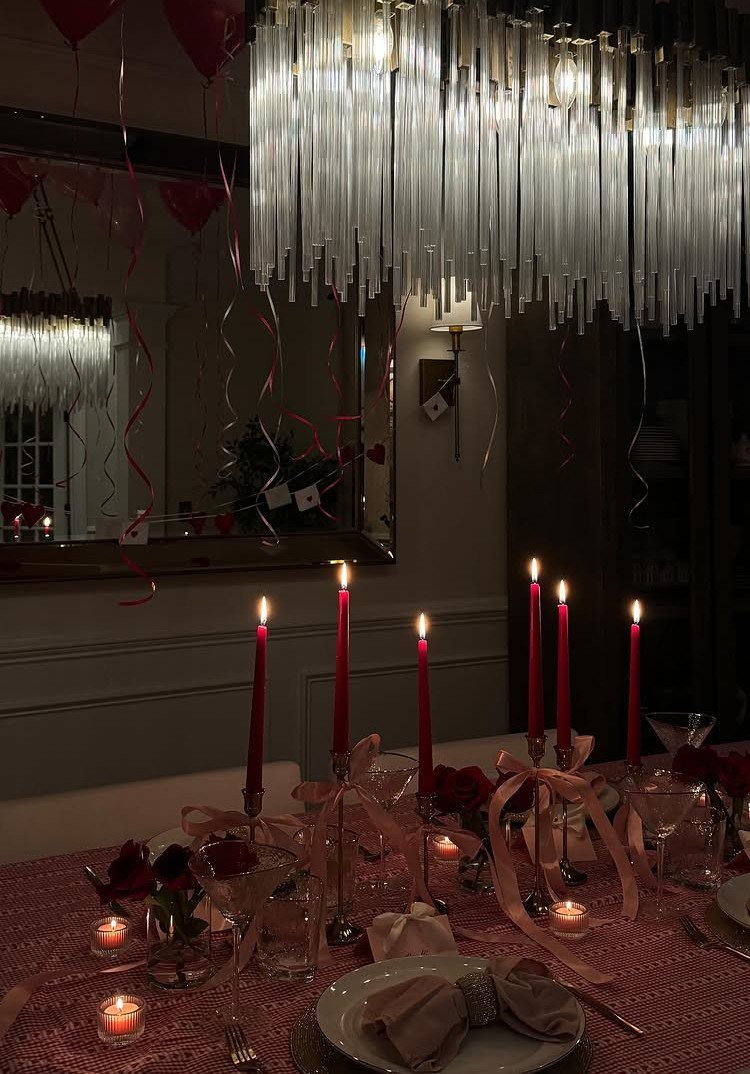 Romantic dinner table setting with red candles, roses, and a crystal chandelier.