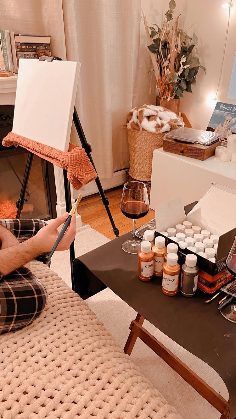 Person painting on a canvas with a glass of red wine nearby.