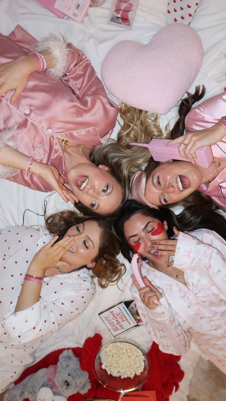 Four women in pink pajamas lying in a circle on a white bed.