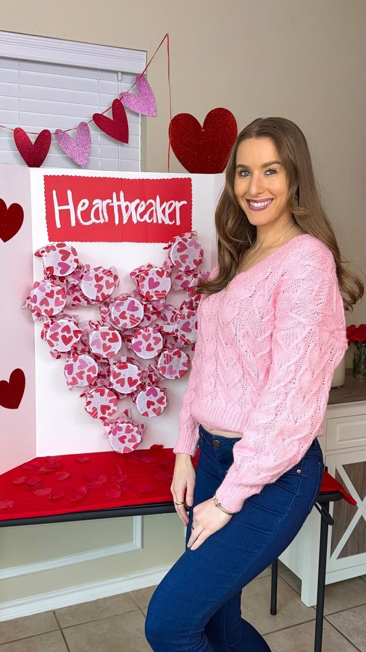 Woman posing next to a Valentine's Day themed photo booth backdrop with paper hearts.