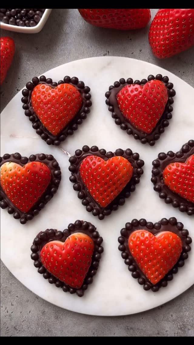 Heart-shaped chocolate treats with fresh strawberries on a white marble platter
