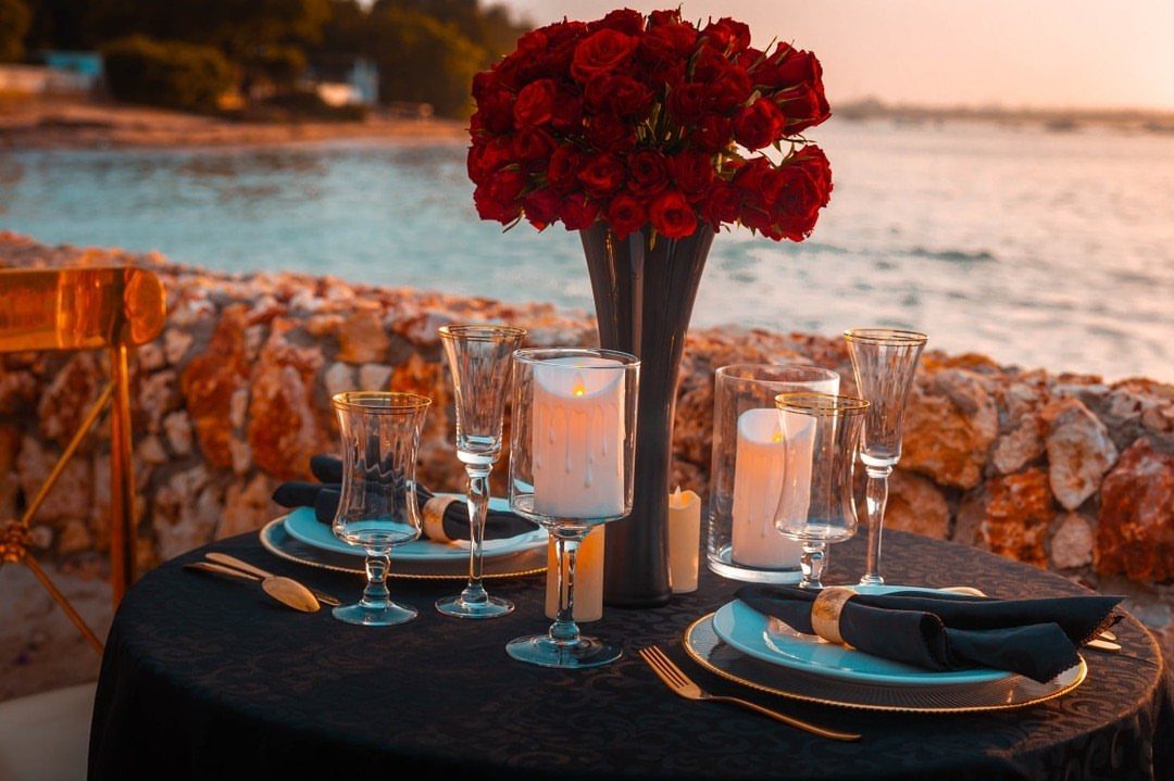 Romantic dinner table with red roses and candles overlooking the ocean at sunset.