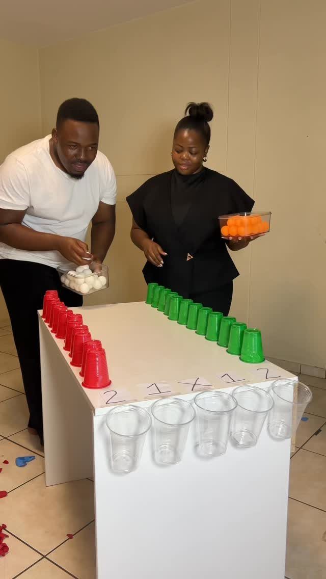 Couple playing a cup and ball game at a white table indoors