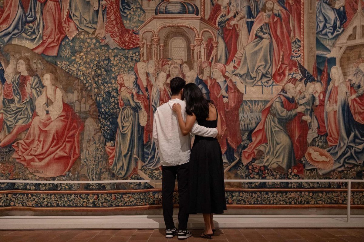 Couple embracing while viewing a large classical tapestry in an art museum gallery.