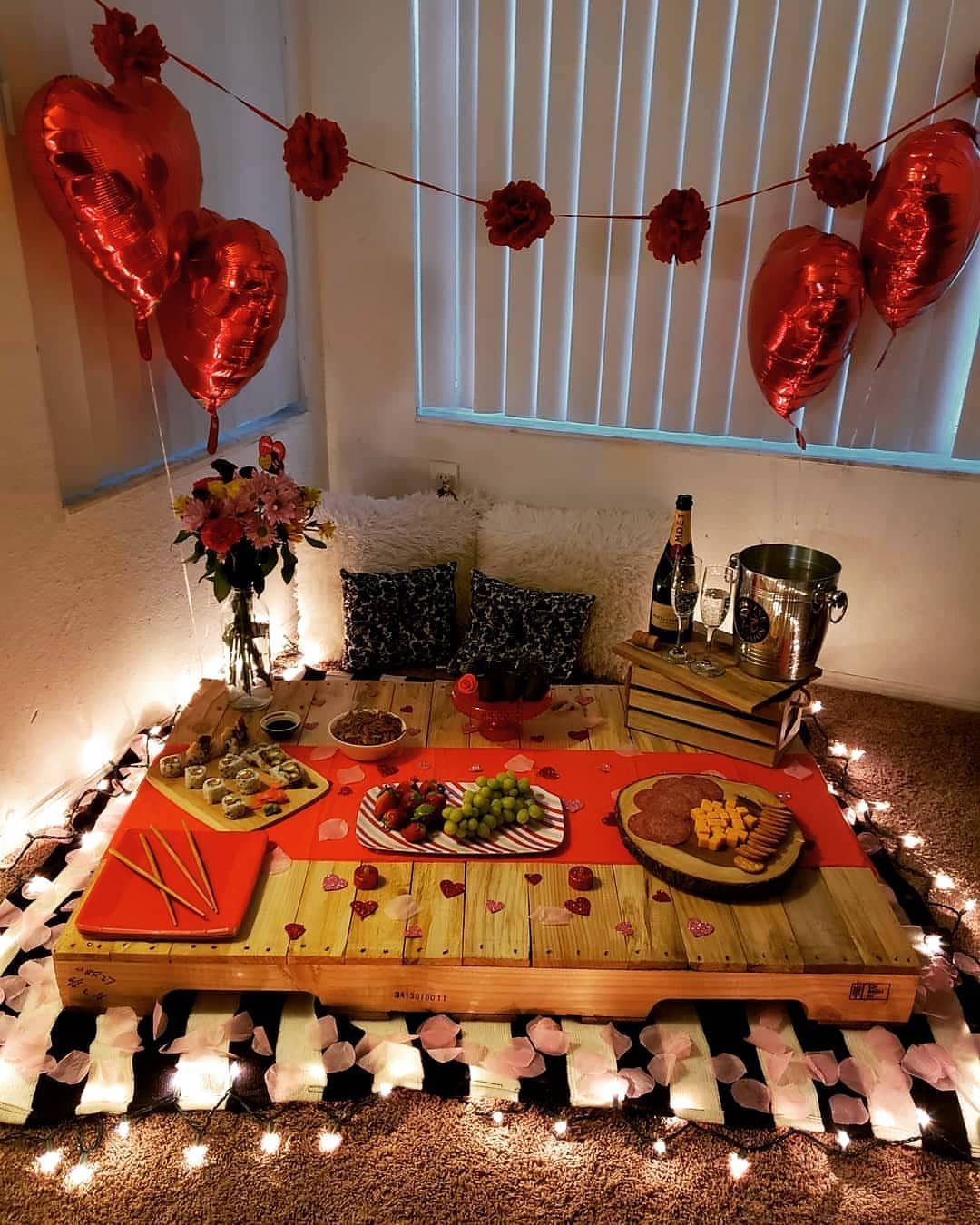 Indoor picnic setup with a pallet table, charcuterie, wine, and red heart balloons.