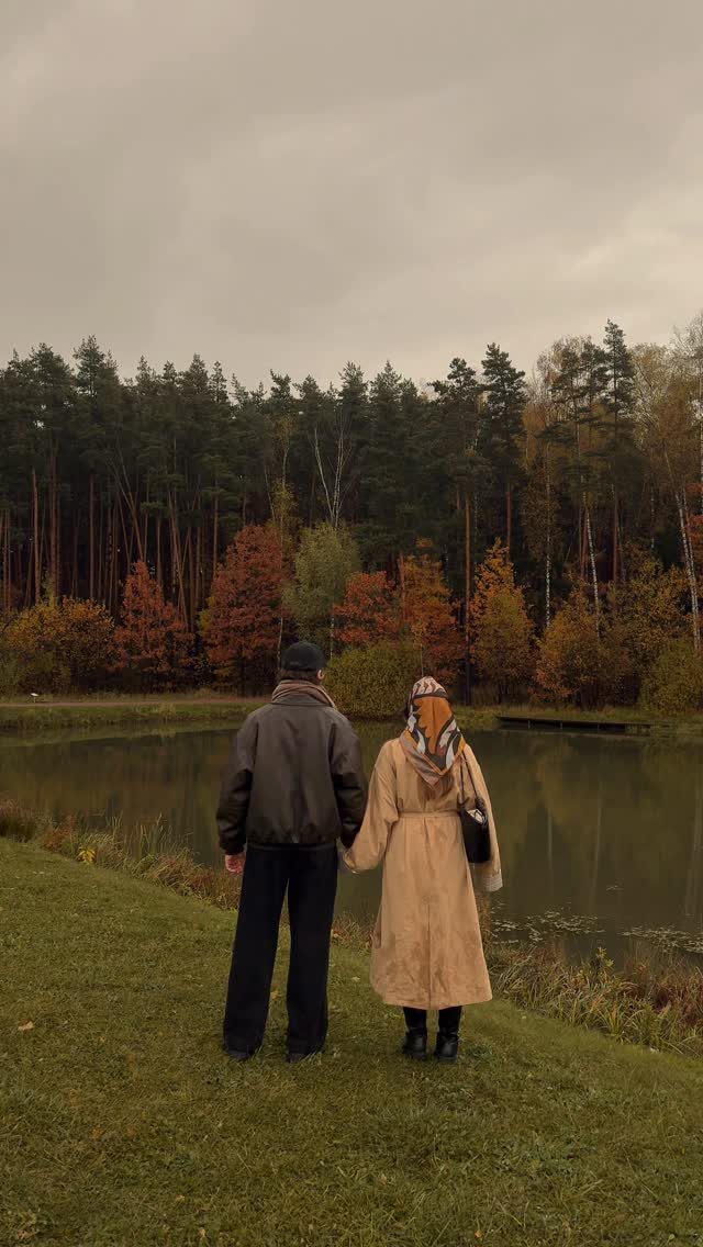 Couple holding hands while looking at a pond surrounded by autumn forest trees.