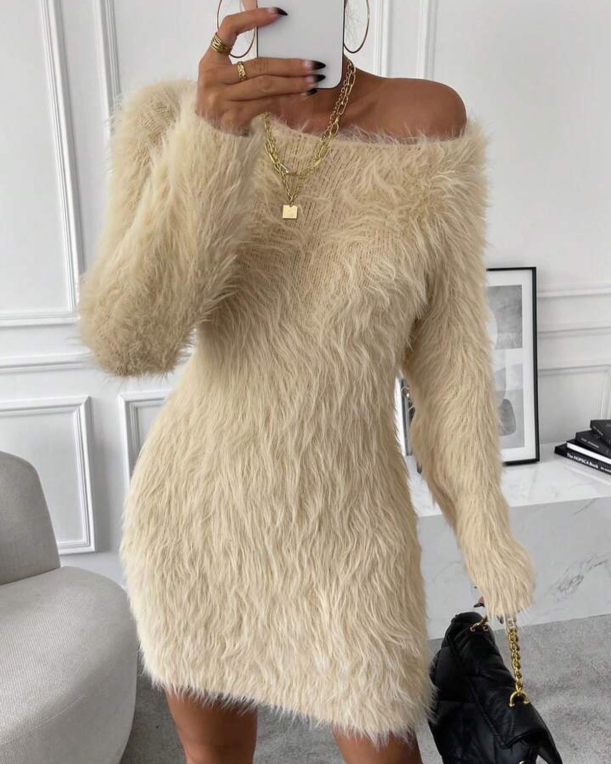 Person in a fuzzy cream sweater dress and gold chain necklace taking a selfie.