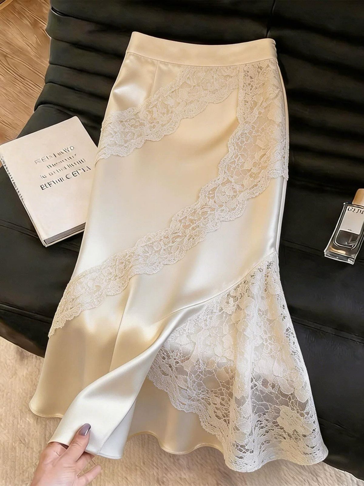 Cream satin slip skirt with intricate lace panels laid on black leather surface.