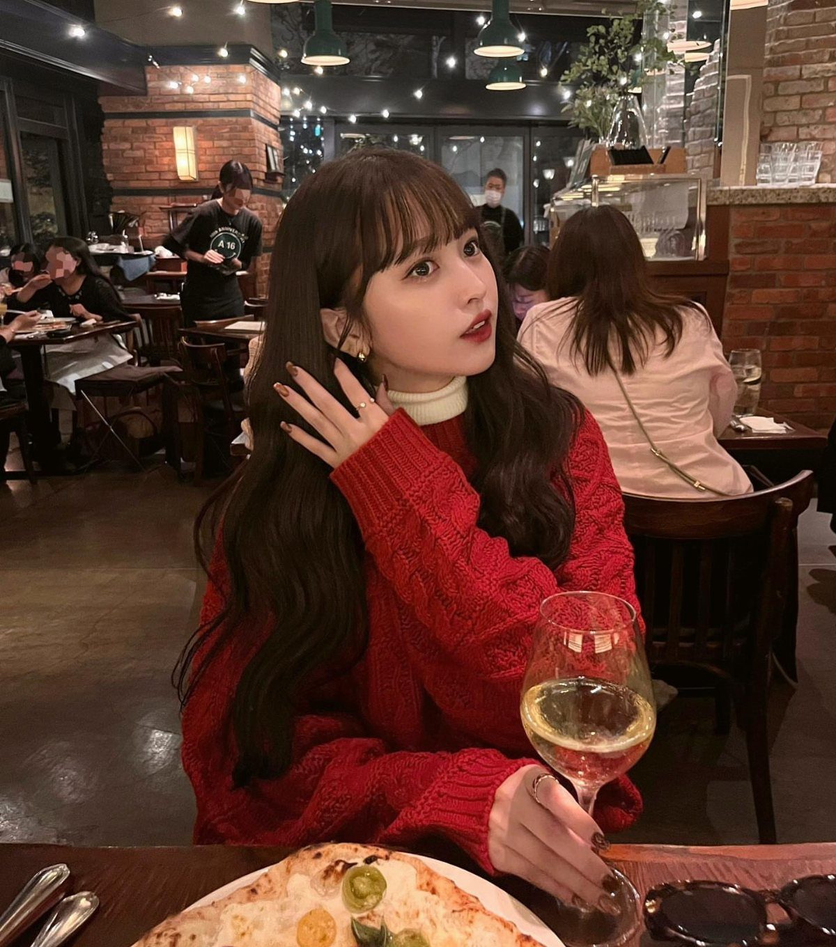 Woman in a red knit sweater sitting at a restaurant with wine and pizza.
