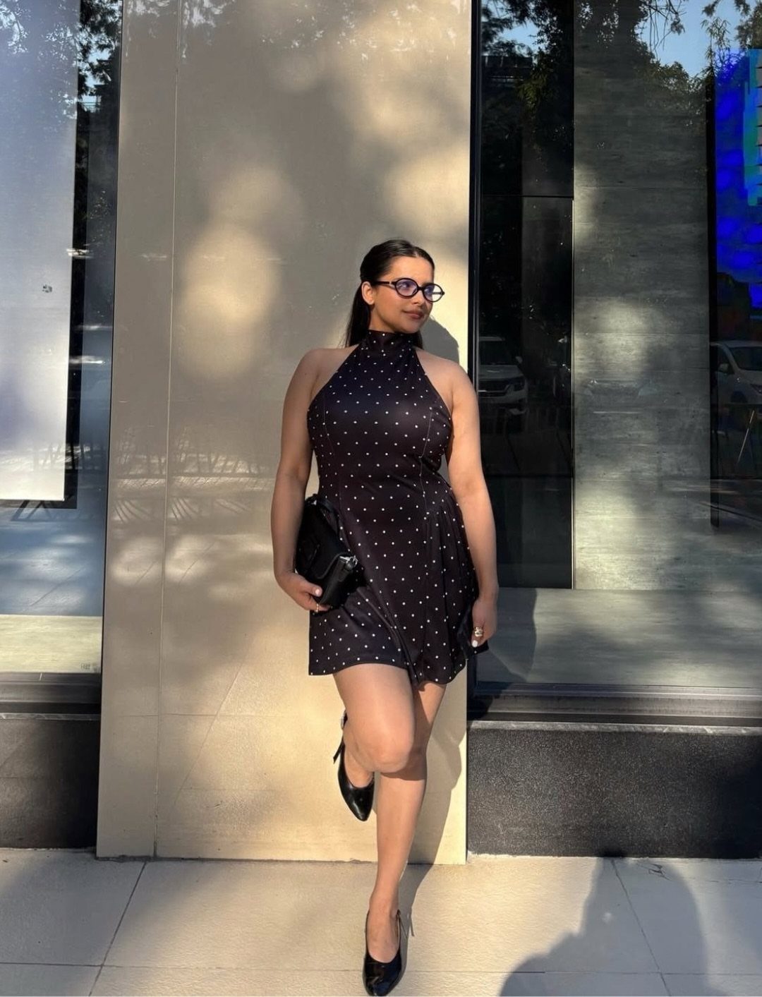 Woman in a black polka dot halter dress and black heels posing outdoors.