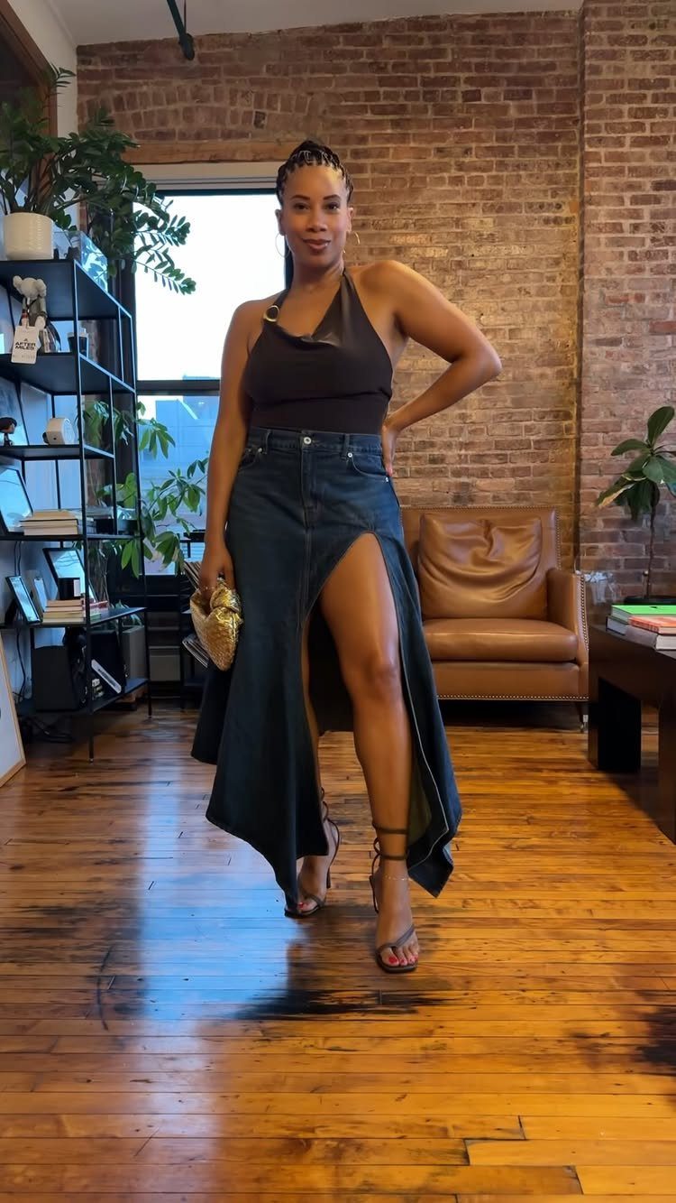 Woman wearing a black halter top and long denim skirt with high slit.