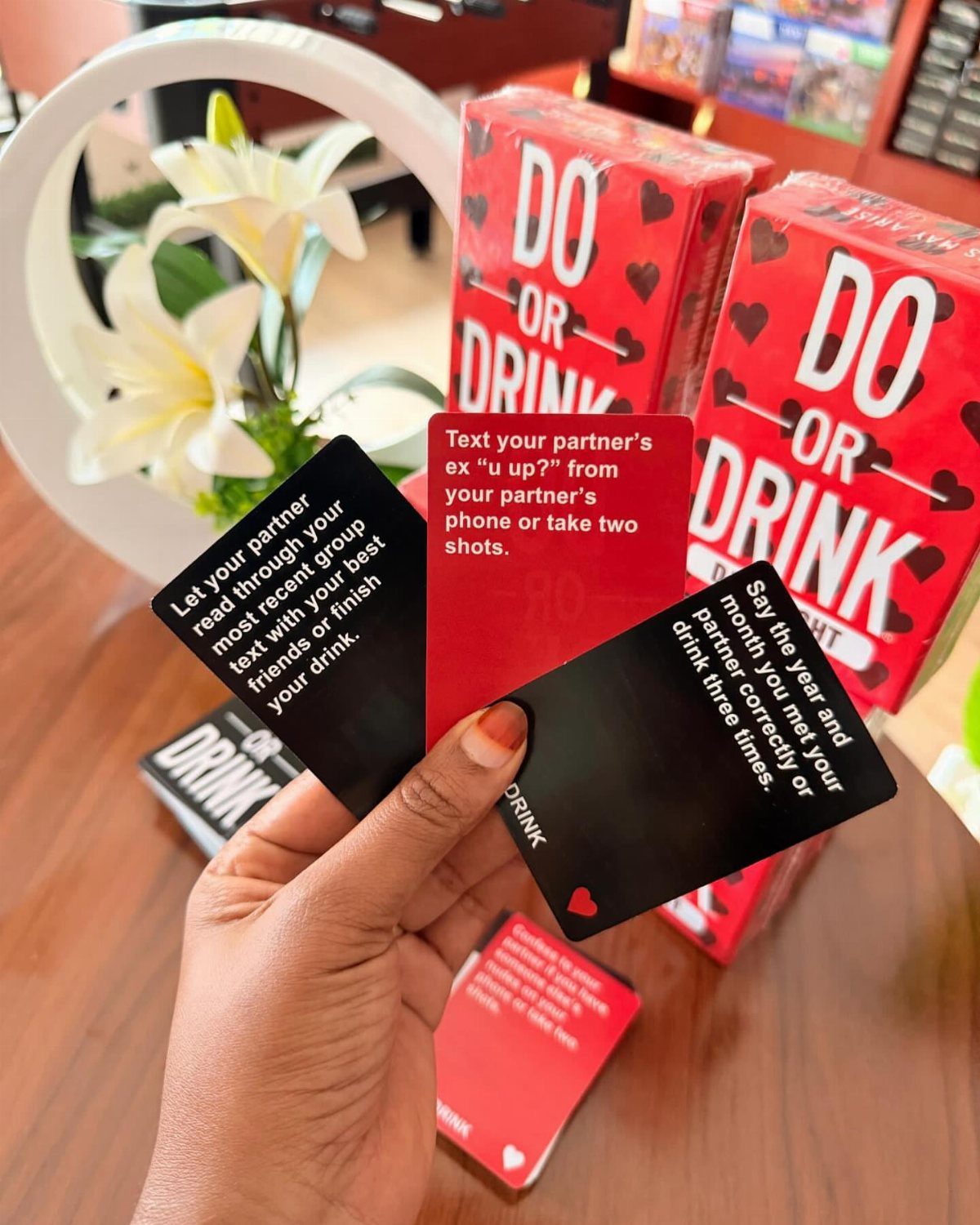 Hand holding Do or Drink game cards with red game boxes and lilies.