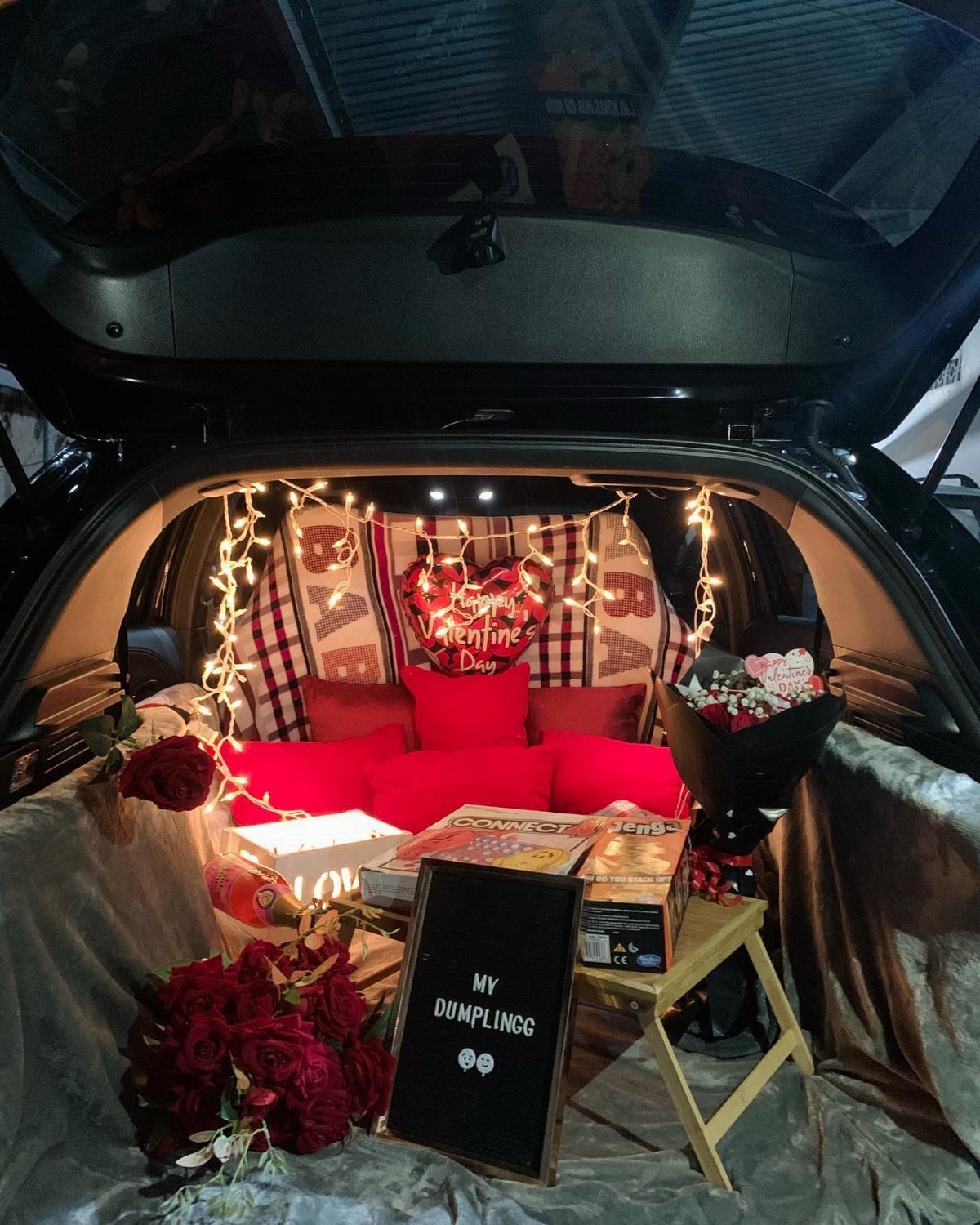 Decorated car trunk with red pillows, roses, and fairy lights for Valentine's Day.