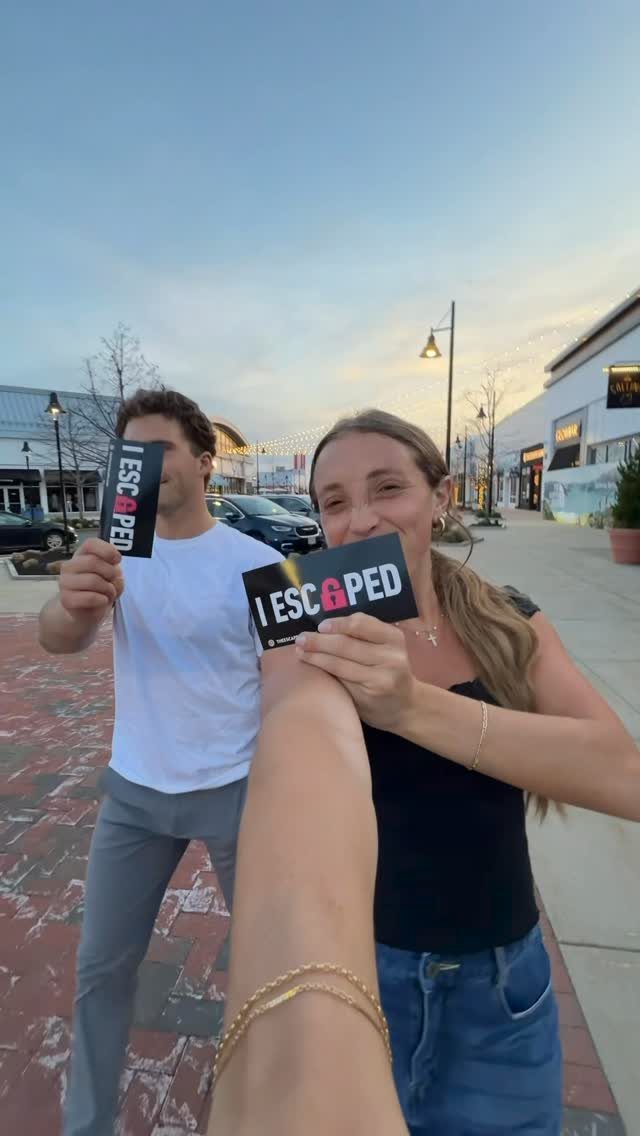 Couple holding I ESCAPED signs after completing an escape room challenge outdoors.