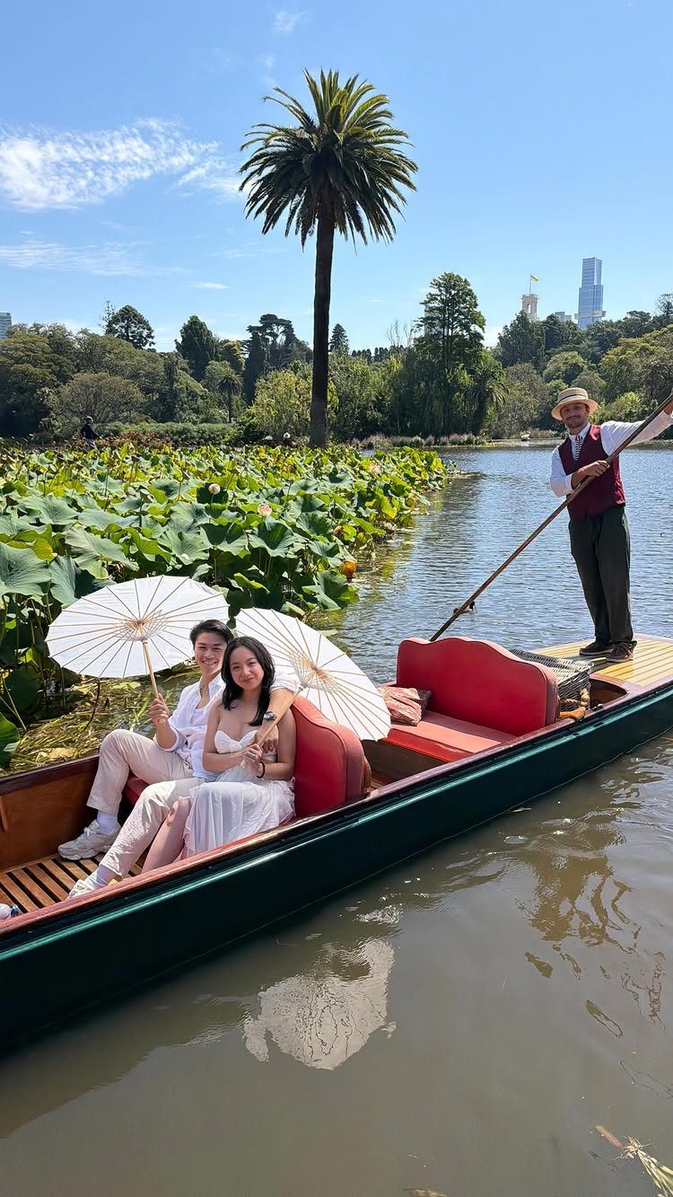 Couple in white clothing riding a boat through a lush botanical garden pond.