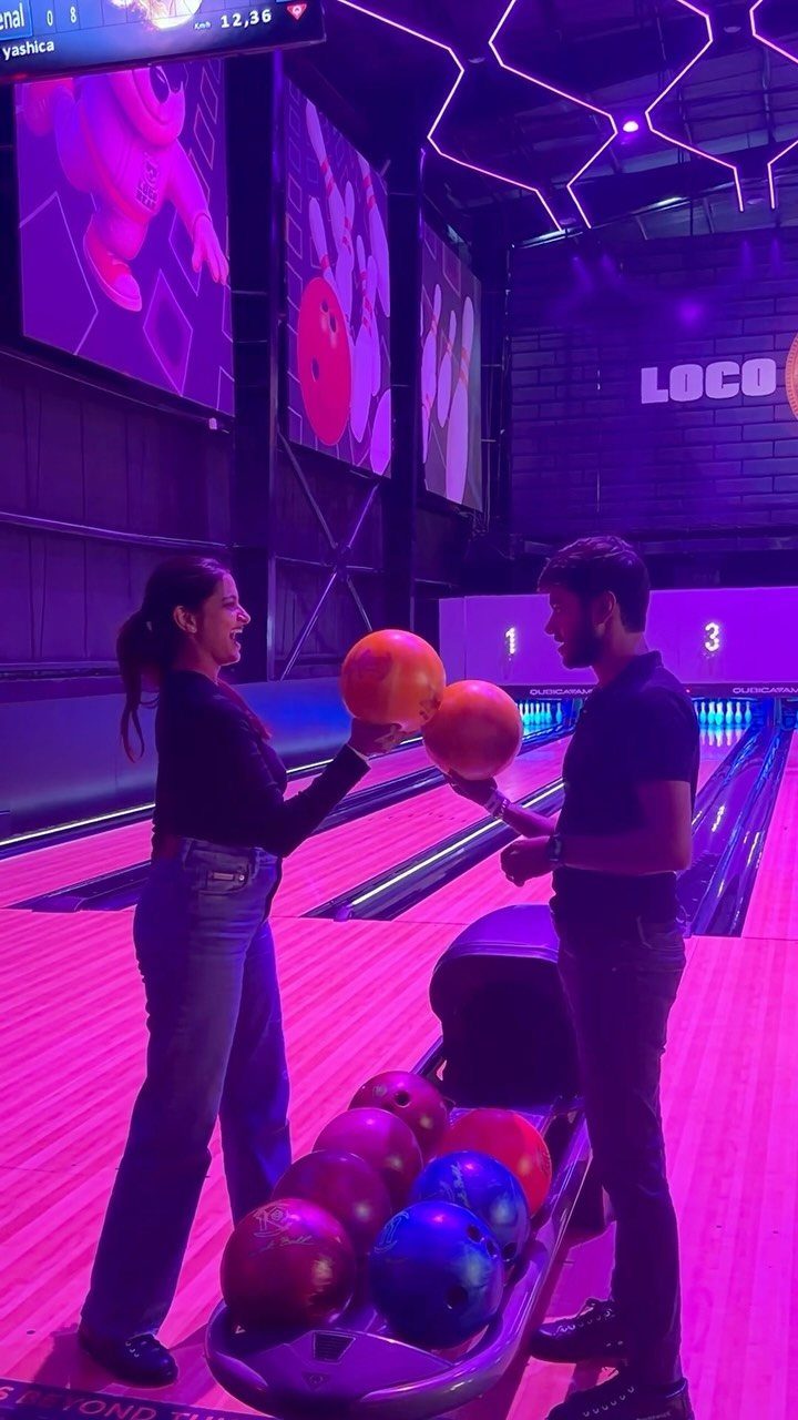 Man and woman holding orange bowling balls on a purple neon bowling lane.