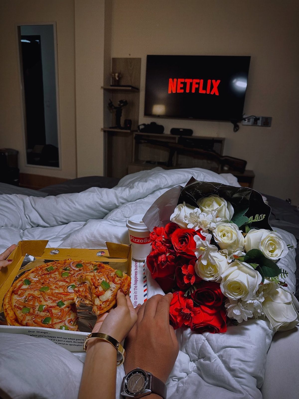 Pizza and roses on a bed with Netflix playing on a television screen.