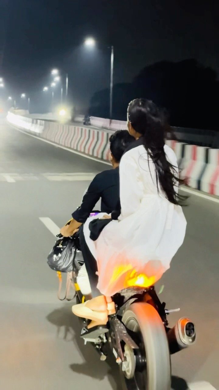Couple riding a motorcycle together on a lit road at night