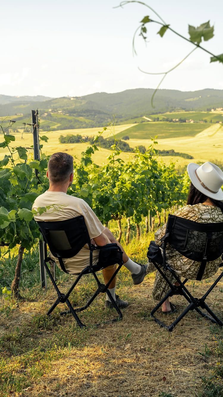 Couple sitting in folding chairs overlooking a scenic vineyard and rolling hills.