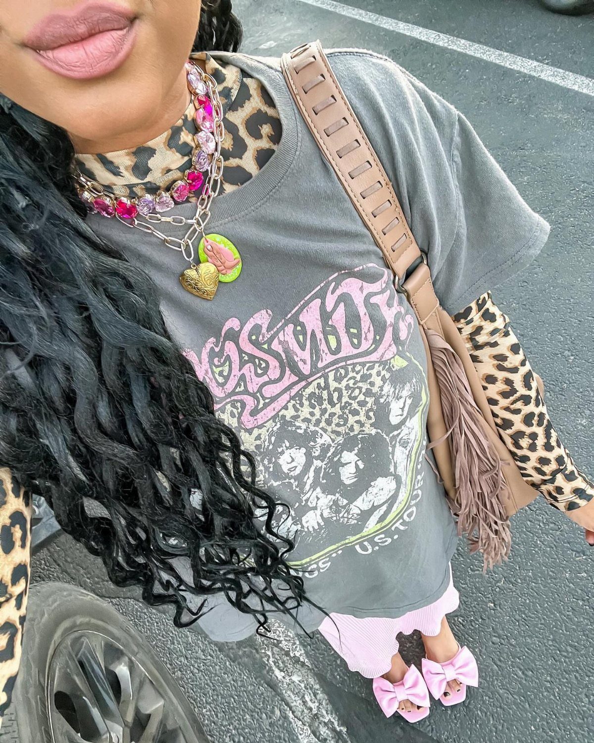 Person wearing layered colorful necklaces, a graphic tee, and pink bow sandals.