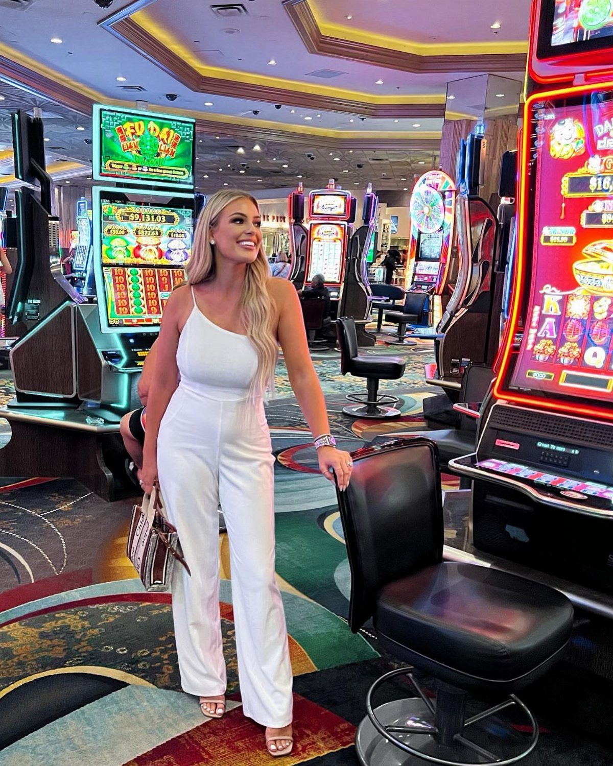 Woman in a white sleeveless jumpsuit posing inside a colorful Las Vegas casino.