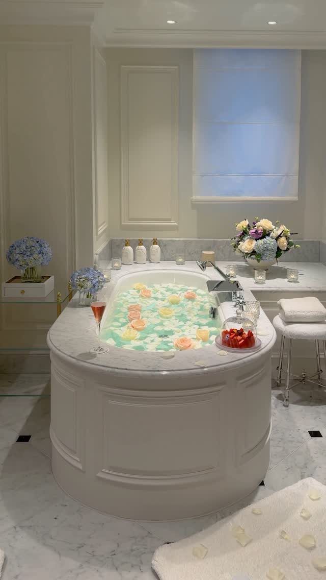 Marble bathtub with floating petals, champagne, and strawberries in a luxury bathroom.