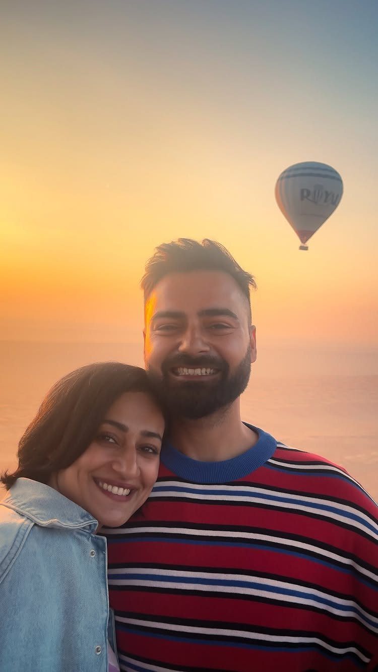 Smiling couple posing together at sunset with a hot air balloon in the background