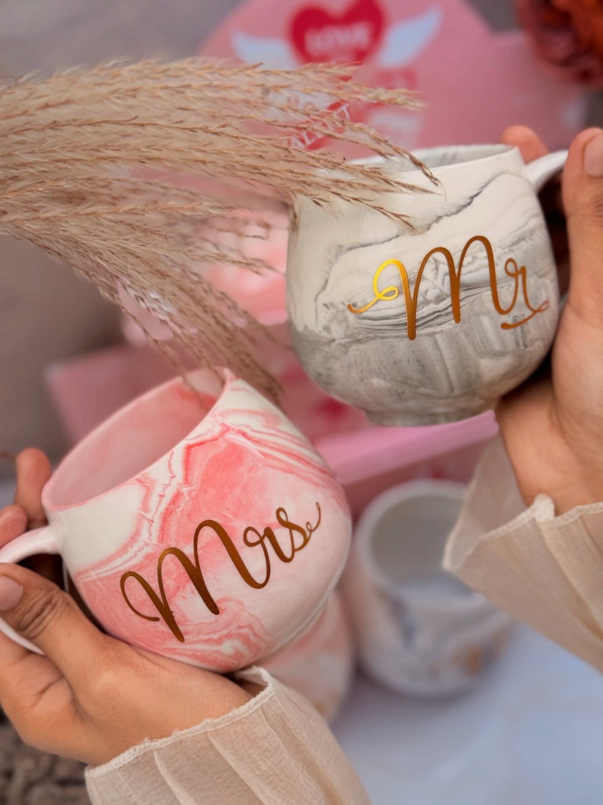 Two marbled ceramic mugs with gold Mr. and Mrs. lettering held by hands.