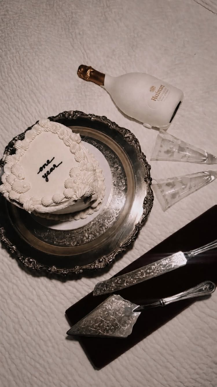 Heart-shaped white cake with one year text, champagne bottle, and silver serving tools.
