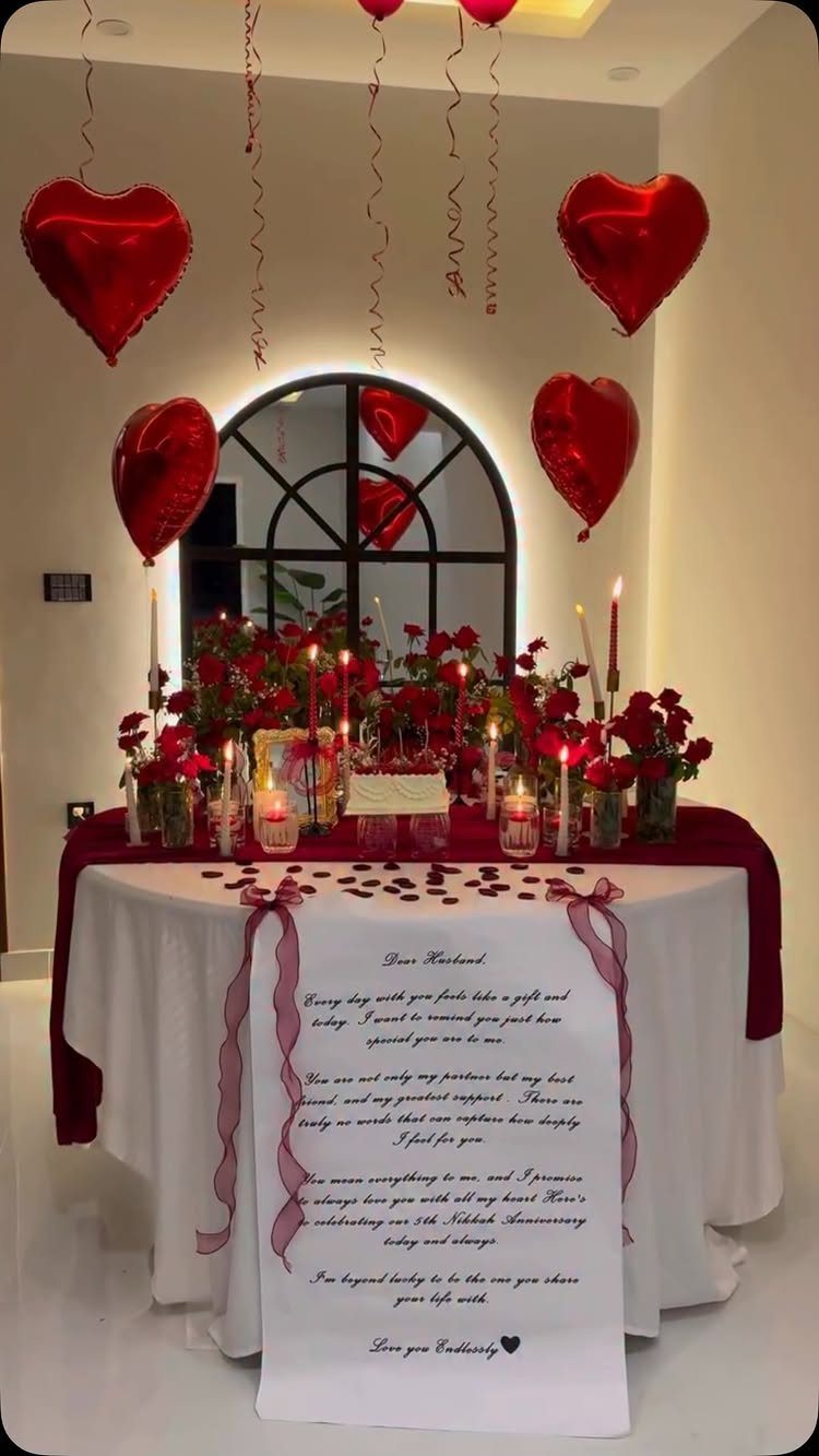 Romantic table setting with red roses, candles, heart balloons, and a love letter.