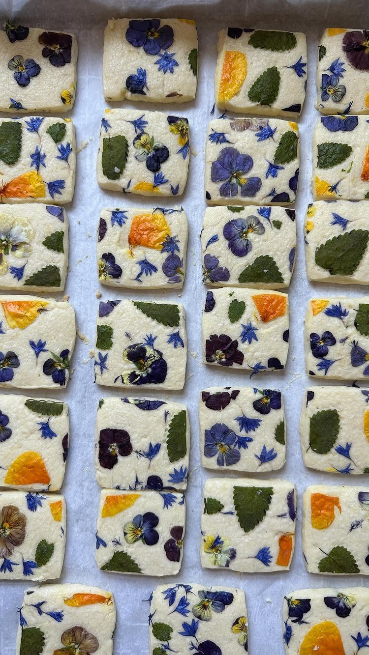 Square white cookies decorated with colorful pressed edible flowers on a baking sheet