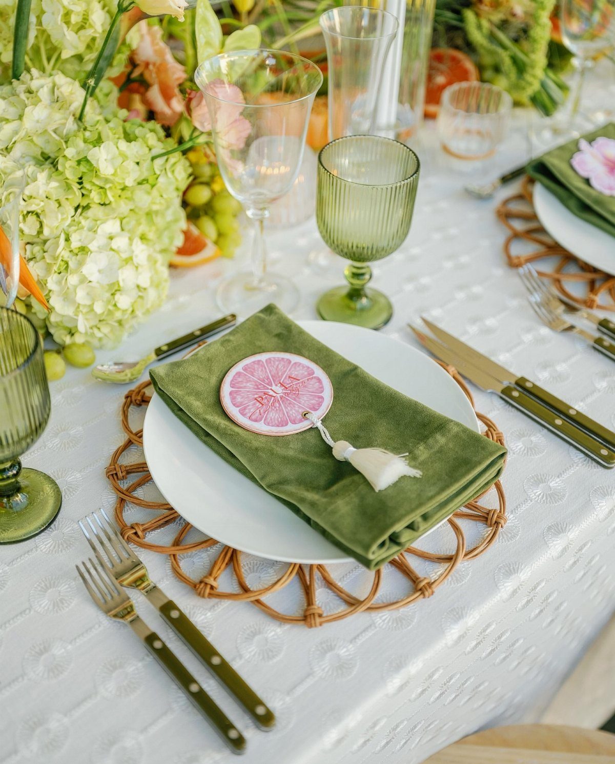 Wedding table setting with green napkins, rattan chargers, and citrus-themed place cards.