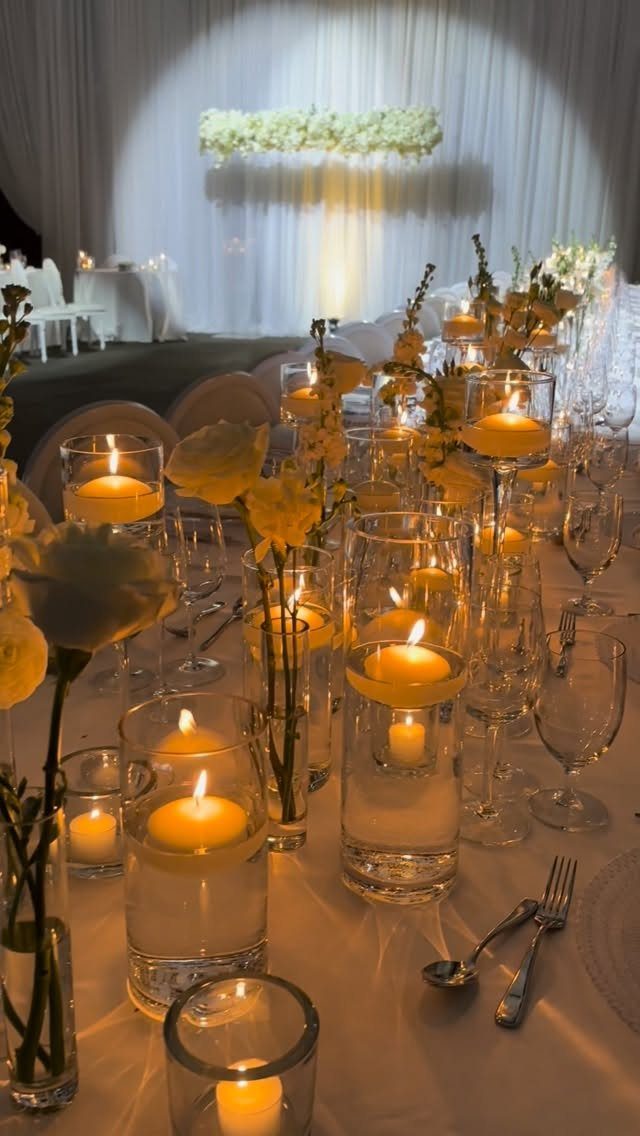 Floating yellow candles in glass cylinders with yellow flowers on a wedding table.