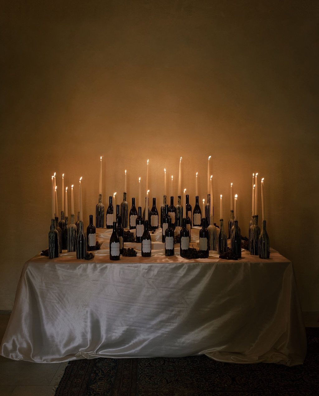 Dark glass bottles used as candle holders with lit taper candles on a table.