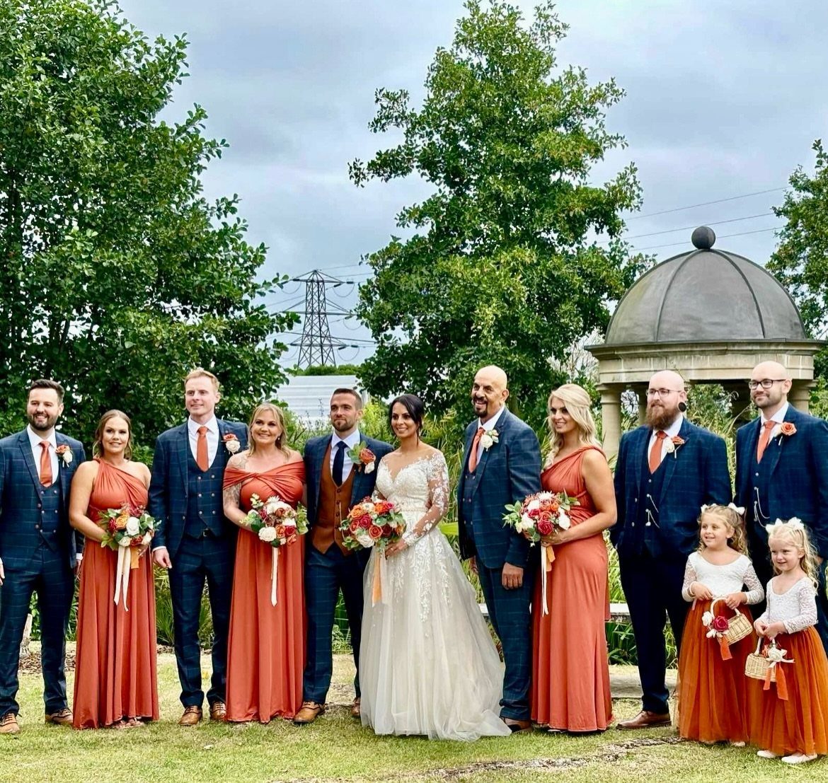 Wedding party with bridesmaids in burnt orange dresses and groomsmen in navy suits.