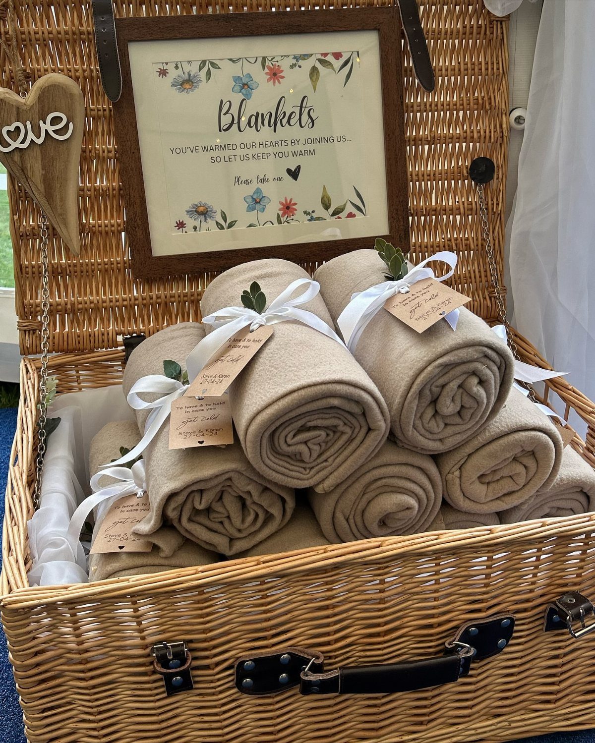 Rolled tan blankets with white ribbons inside a woven wicker basket with sign