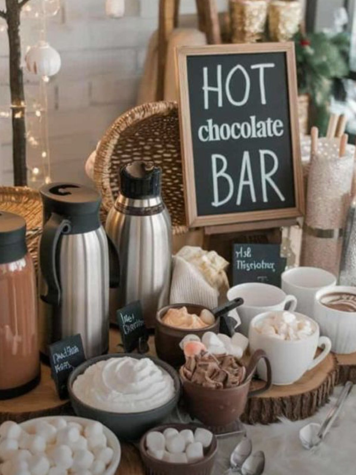 Hot chocolate bar with thermoses, mugs of cocoa, and a chalkboard sign.