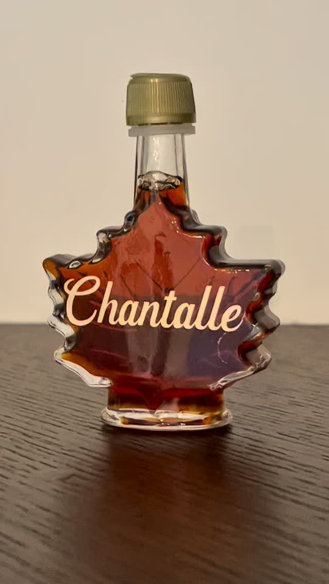 Maple leaf-shaped glass bottle of syrup with personalized name on dark wood surface