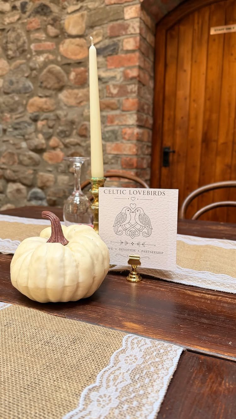 White pumpkin and taper candle on a rustic wooden table with burlap runner.